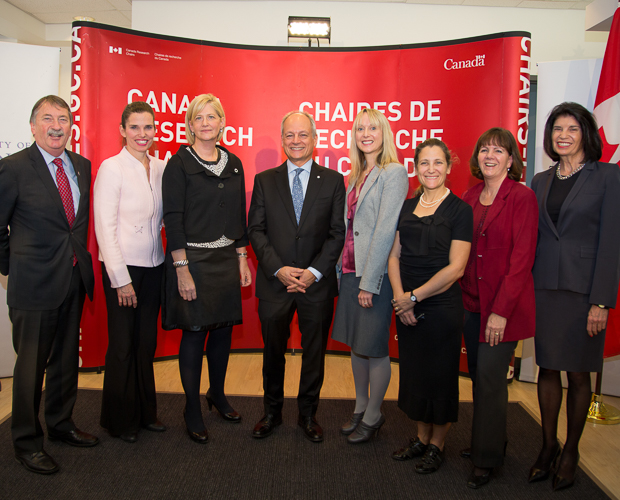 Meric Gertler poses for a photo with 7 men and women. Behind them, a banner reads, Canada Research Chairs.