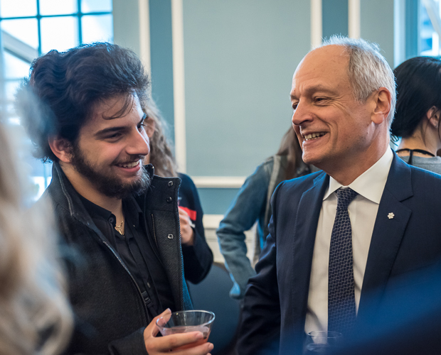 Meric Gertler and a young man laugh as they talk together at a reception.